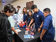 Students stand next to a table with a computer and The Claw prototype.