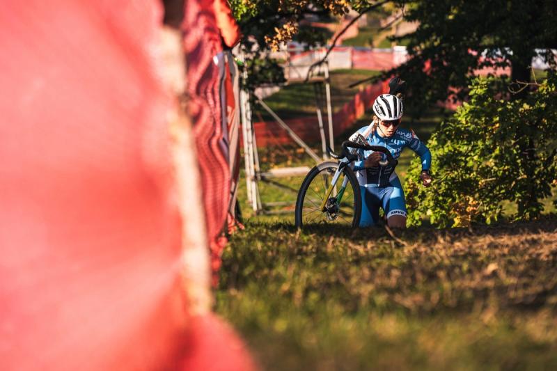 Mladý závodník v modrém běží s kolem přes travnatý úsek — Cyklokros Chýnov 2026, JANEV Cup, foto Martin Kozojed