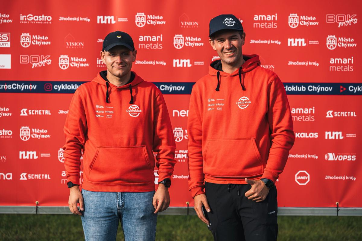 Pořadatelé z Cykloklubu Chýnov v klubových mikinách před stěnou partnerů