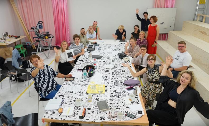 Группа людей сидит вокруг стола, на котором перед ними стоит произведение искусства.