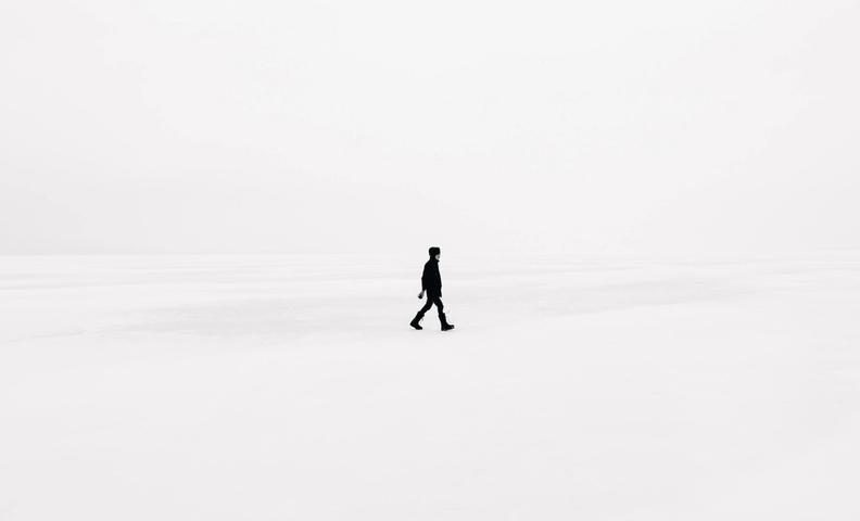 Человек в темной одежде идет по полностью белому фону