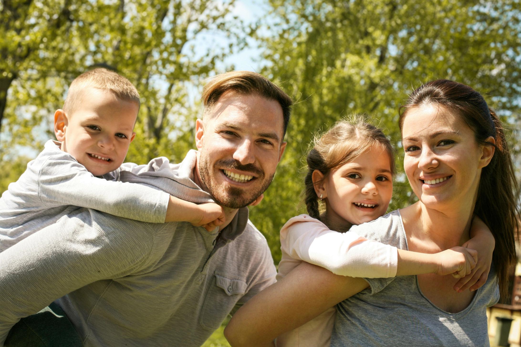 Global: Smilende familie i en solfylt park. En gutt rir på ryggen til faren, og en jente med flette rir på ryggen til moren.