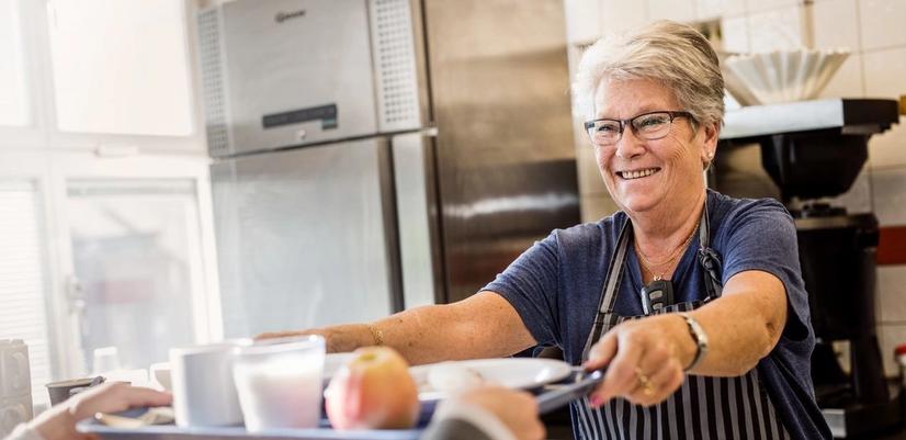 A smiling woman hands out a tray of food.