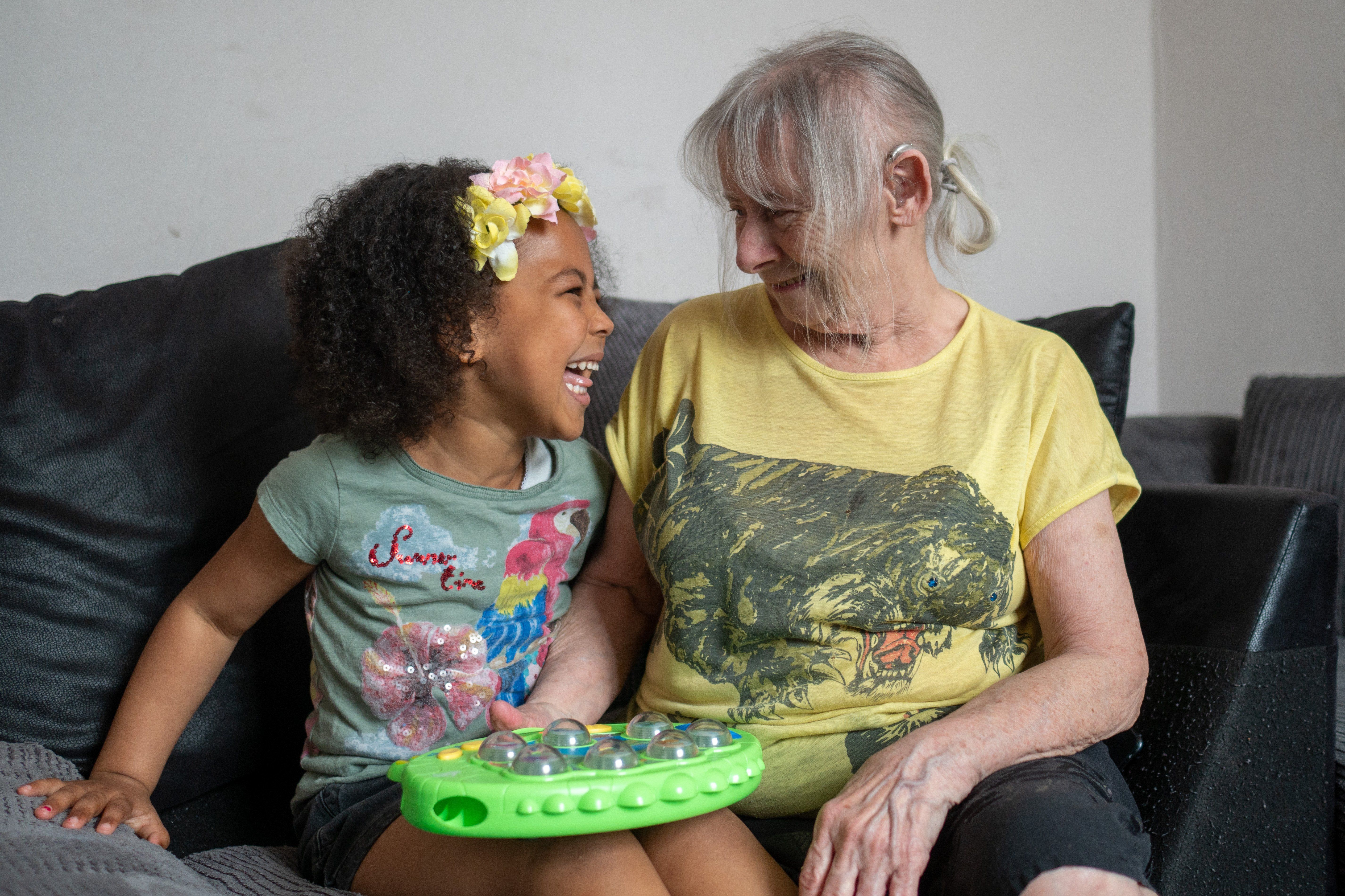 jente med eldre dame som sitter på en sofa og ser på hverandre med kjærlig blikk mens de smiler 