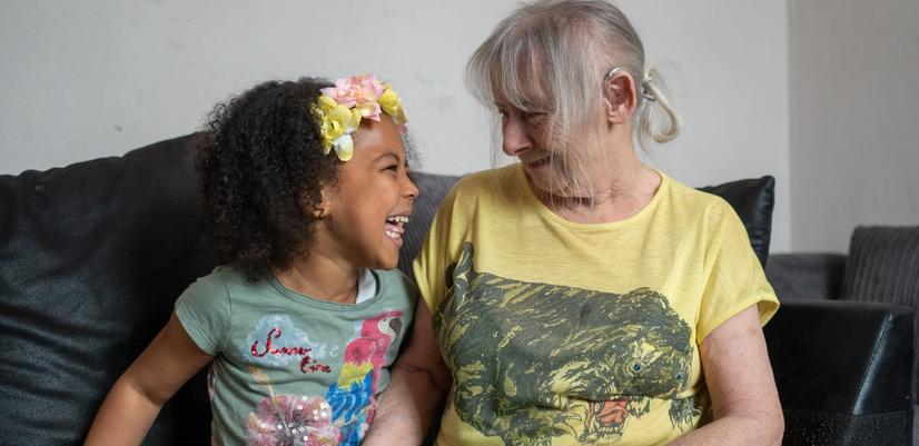 jente med eldre dame som sitter på en sofa og ser på hverandre med kjærlig blikk mens de smiler