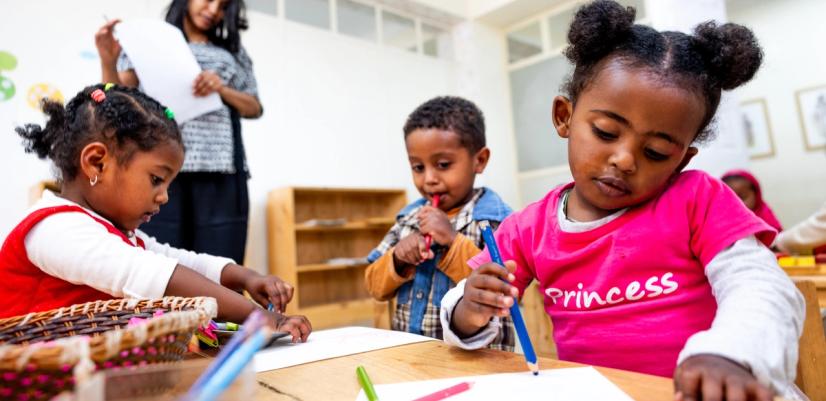 Tre barn i 3-5 års alderen sitter med bordet og tenger