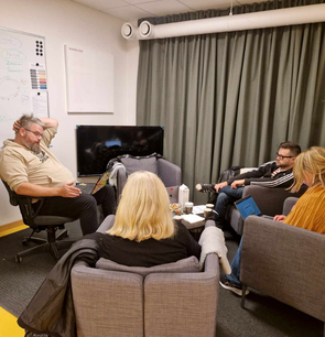 Fire voksne som sitter i et lite rom med gardinene trukket for
