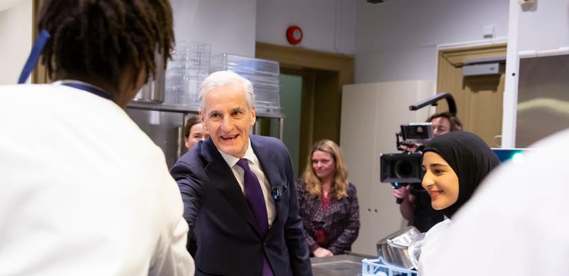De unge kokkene møter statsministeren: Statsminister Jonas Gahr Støre på besøk på kjøkkenet. Smilende håndhilser han på en av de unge kokkene.