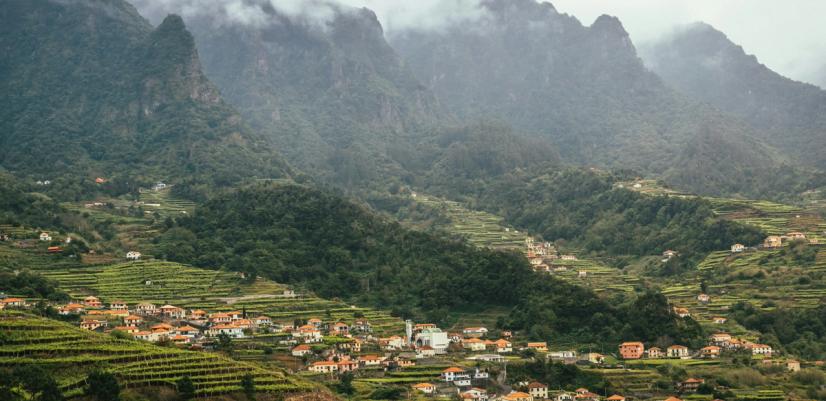 Misty mountain landscape with green terraces, small houses, and a village in a lush valley