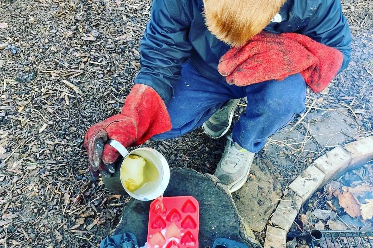 En gutt sitter på bakken og lager mat utendørs. 