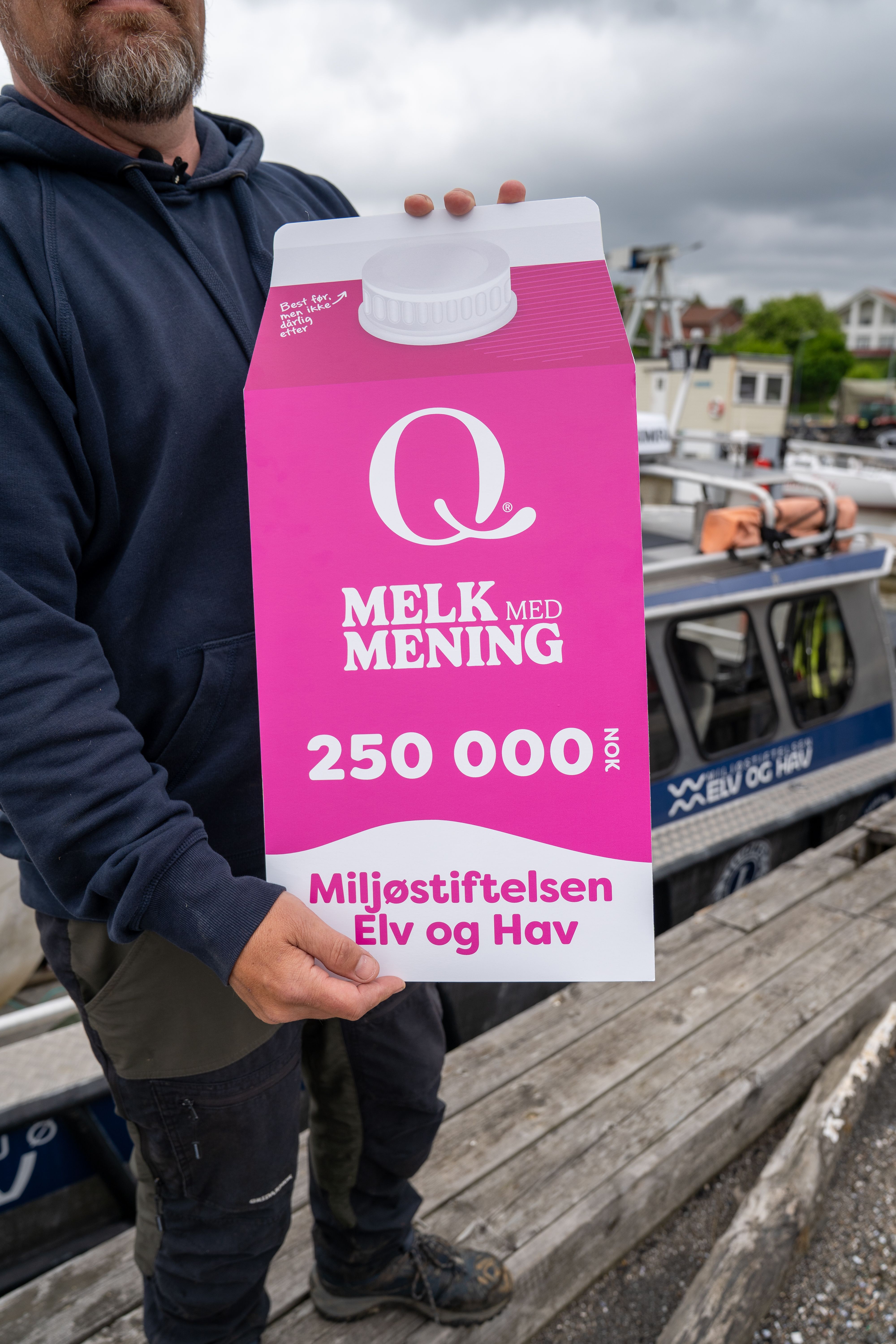 Man håller en rosa skylt med texten "Melk med mening", 250 000 NOK, Stiftelsen Elv og Hav