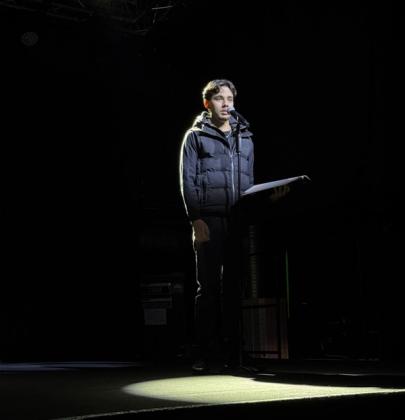 Ungdom står på scenen foran en mikrofon i mørket med lyskaster som lyser på hvam