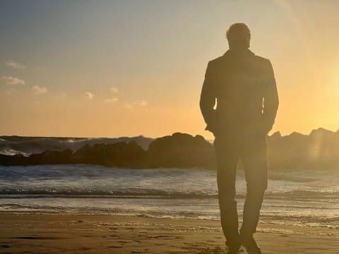 En mann går alene på stranden i solnedgang. 