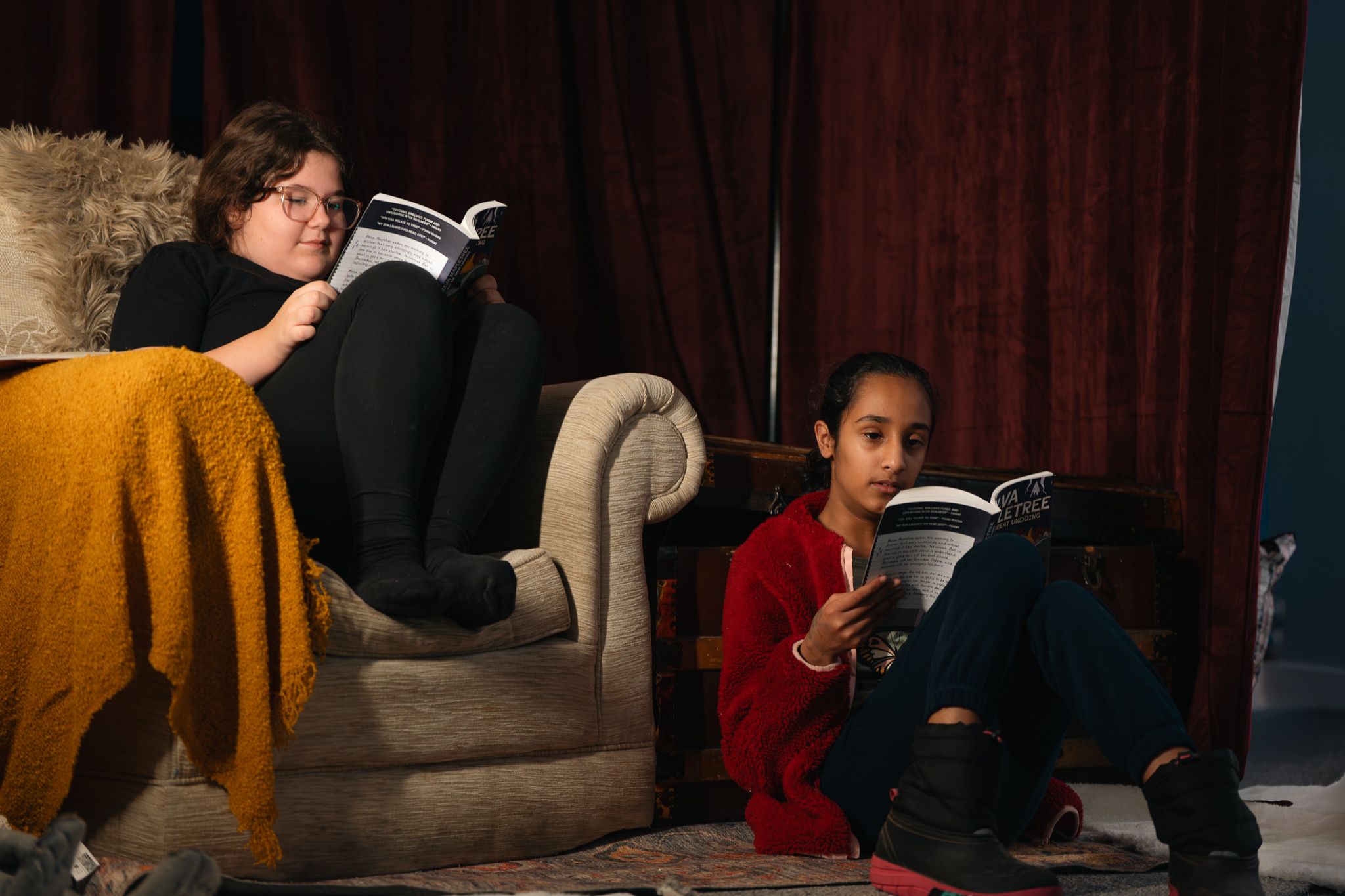 Två barn sitter i ett lugnt rum och läser varsin bok. Bilden visar koncentration, trygghet och läsglädje i en kreativ miljö.