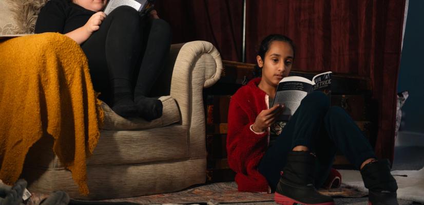 Två barn sitter i ett lugnt rum och läser varsin bok. Bilden visar koncentration, trygghet och läsglädje i en kreativ miljö.