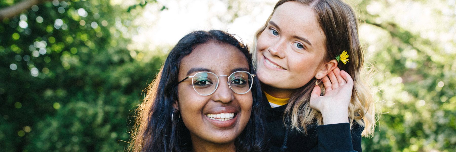 Two teenage girls are smiling at the camera, one with a flower behind her ear.