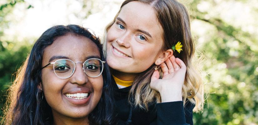 Two teenage girls are smiling at the camera, one with a flower behind her ear.
