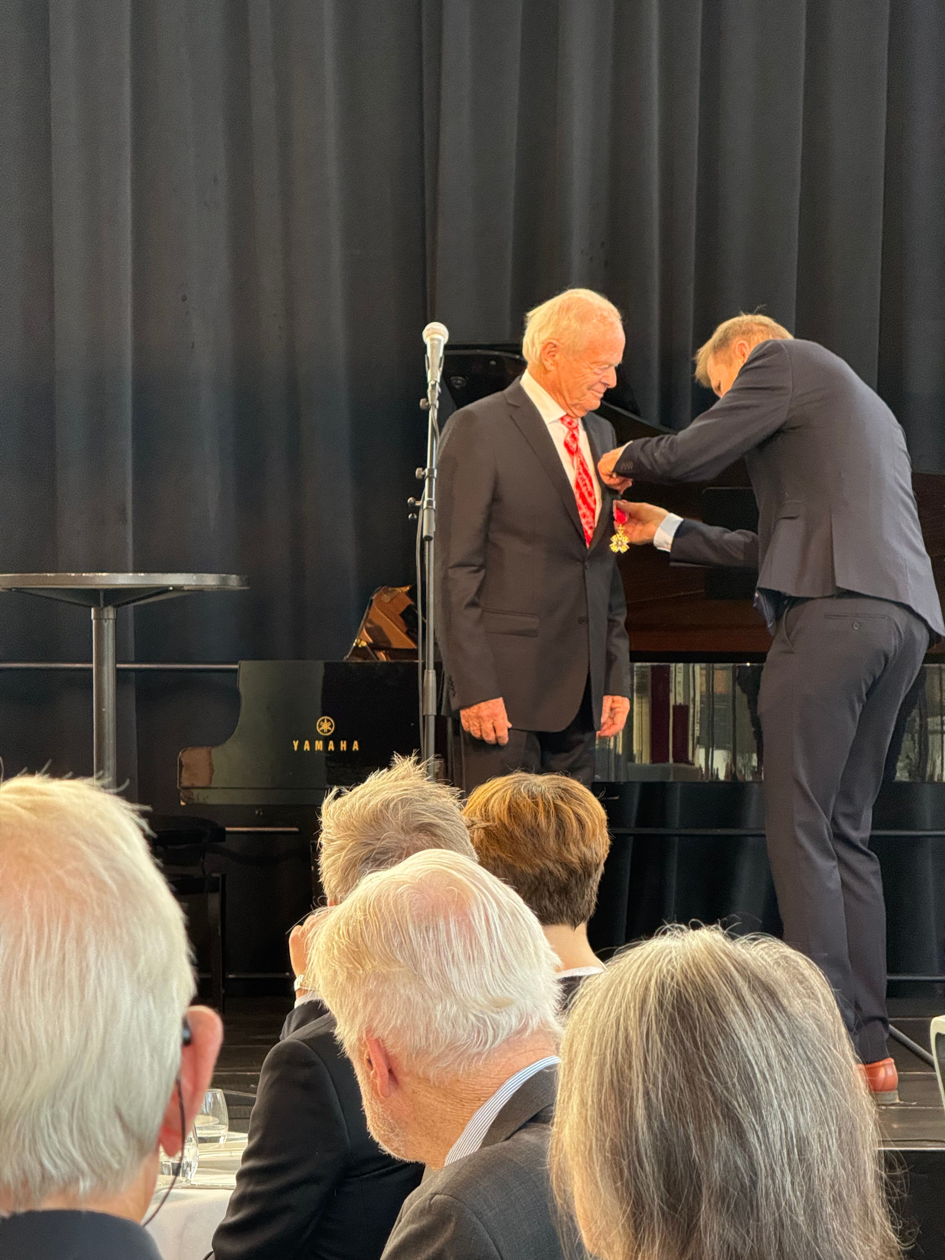 Mann hjelper mann med å feste medalje på brystet på en scene 