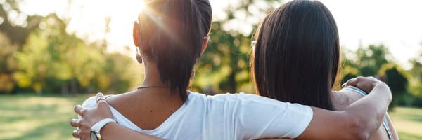 Illustrative photo: Two young girls with their arms around each other, gazing at a sunlit green landscape.
