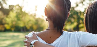 Illustrative photo: Two young girls with their arms around each other, gazing at a sunlit green landscape.