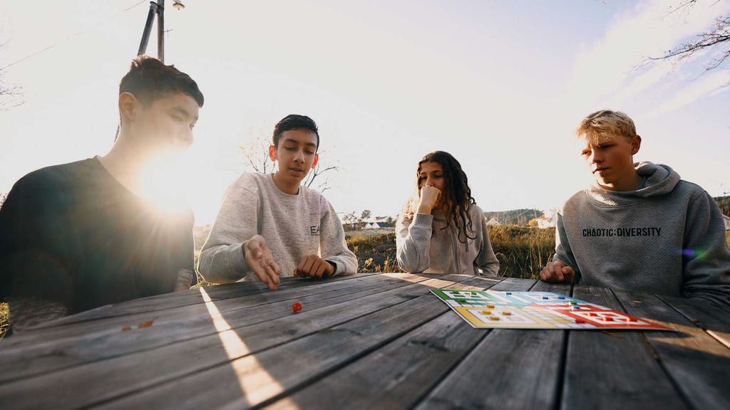 Fyra ungdomar spelar brädspel tillsammans utomhus.