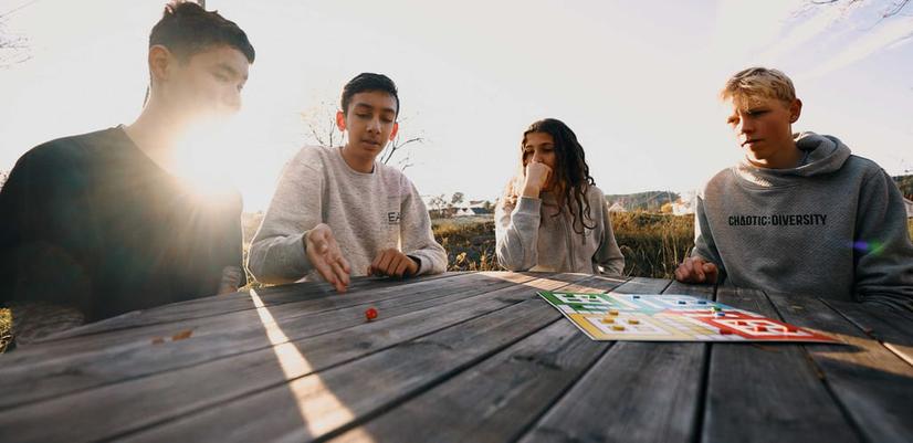 Fyra ungdomar spelar brädspel tillsammans utomhus.