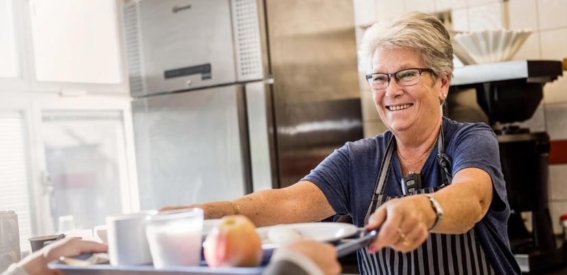 En smilende kvinne deler ut et brett med lunsjmat