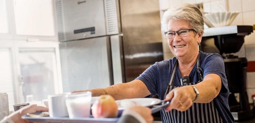 A smiling woman is handing out lunch trays.