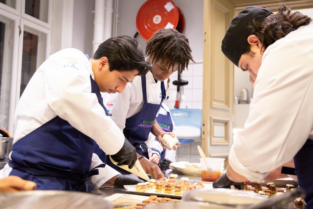 Tre av de unga kockarna jobbar koncentrerat medan de samarbetar för att tillaga mat.