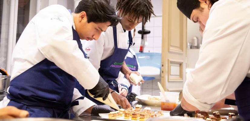 Tre av de unga kockarna jobbar koncentrerat medan de samarbetar för att tillaga mat.