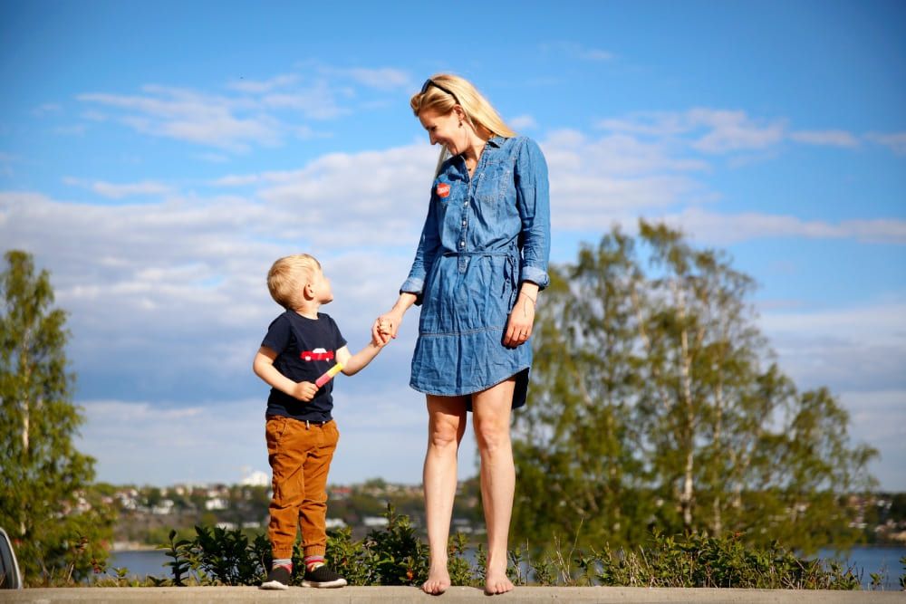 Barn och kvinna håller varandras händer och ler mot varandra en sommardag.