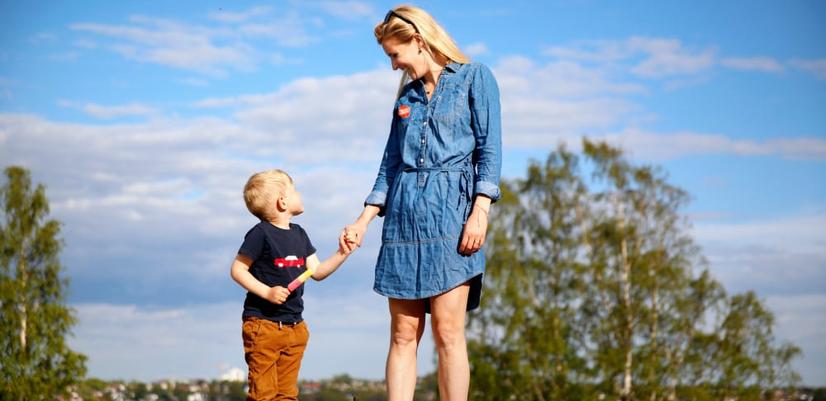 Barn och kvinna håller varandras händer och ler mot varandra en sommardag.