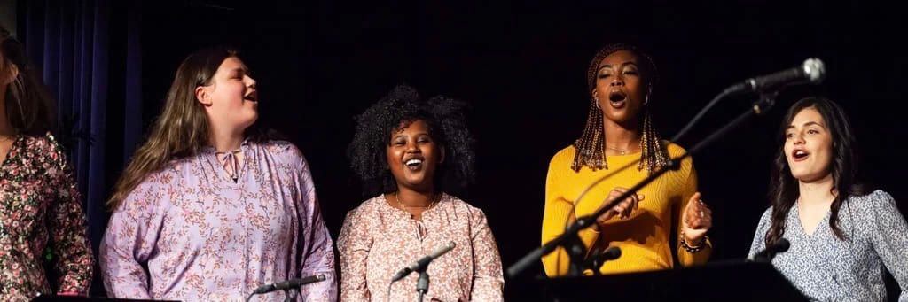 Fem damer synger på en scene