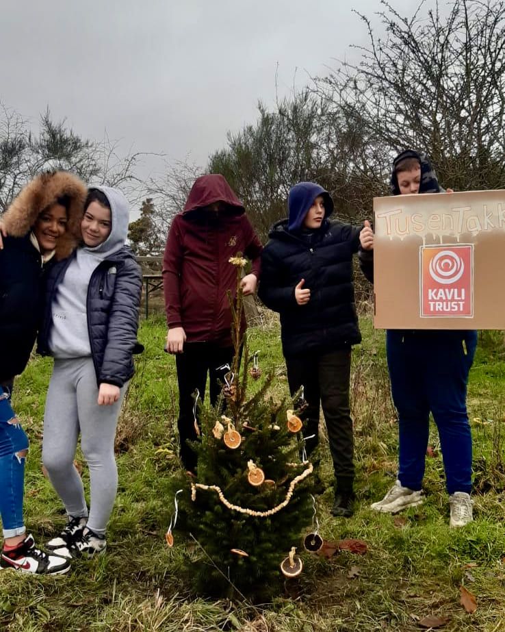 Fem ungdomar står framför en liten norsk julgran som de har planterat och pyntat. De håller upp en skylt med orden ”Tusen tack till Kavlifonden”.