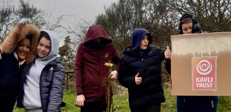 Fem ungdommer står foran en liten norsk julegran de har plantet og pyntet. De holder opp en plakat med ordene 'Tusen takk til Kavlifondet'.