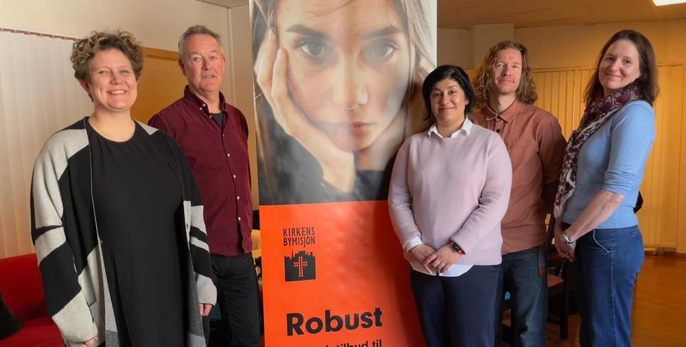 Fem representanter från Ferd SE, Kirkens Bymisjon och Kavlifonden står tillsammans runt en affisch för Robust-projektet.