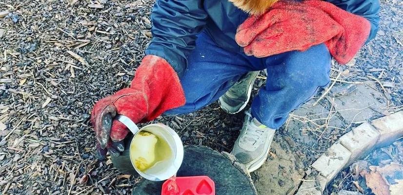 En gutt sitter på bakken og lager mat utendørs.