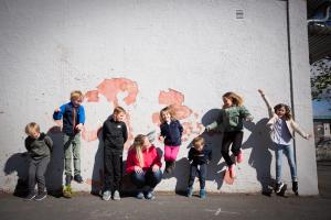 Along a school wall, children jump in a row. The founder of Gleding, Siri Abrahamsen, is sitting in the middle.