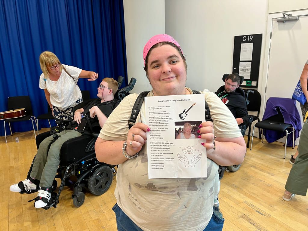 Anna, en av deltakerne i Music Spark, ser i kamera og smiler mens hun holder opp sangteksten som hun har skrevet .