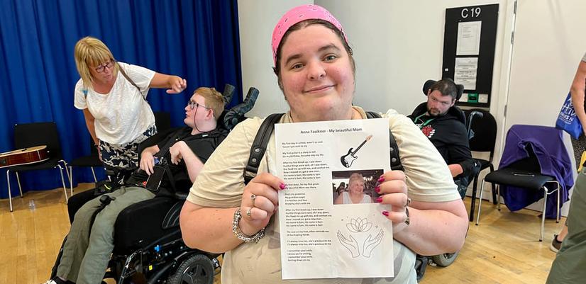 Anna, en av deltakerne i Music Spark, ser i kamera og smiler mens hun holder opp sangteksten som hun har skrevet .