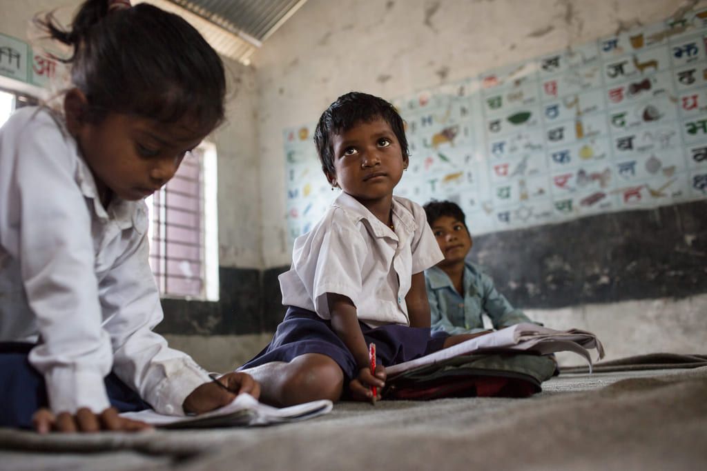 Three children sit on the floor doing school work at Yanasewa Primary School.