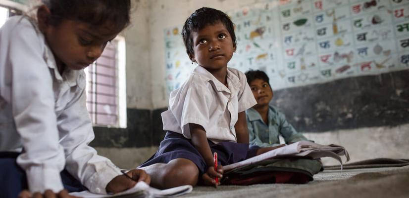 Three children sit on the floor doing school work at Yanasewa Primary School.