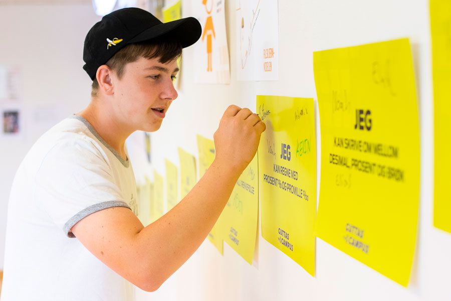 En ungdom med caps skriver på en vegghengt plakat