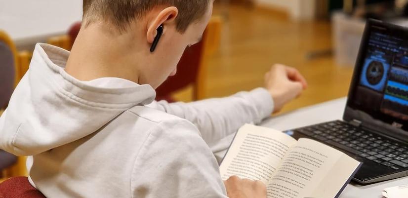 En gutt sitter konsentrert og leser i en bok.