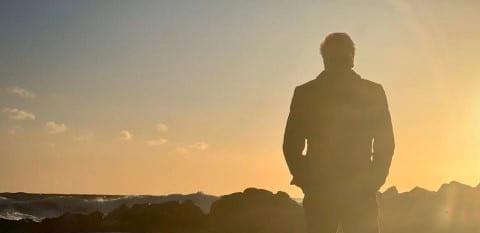 A man walks alone on the beach at sunset.
