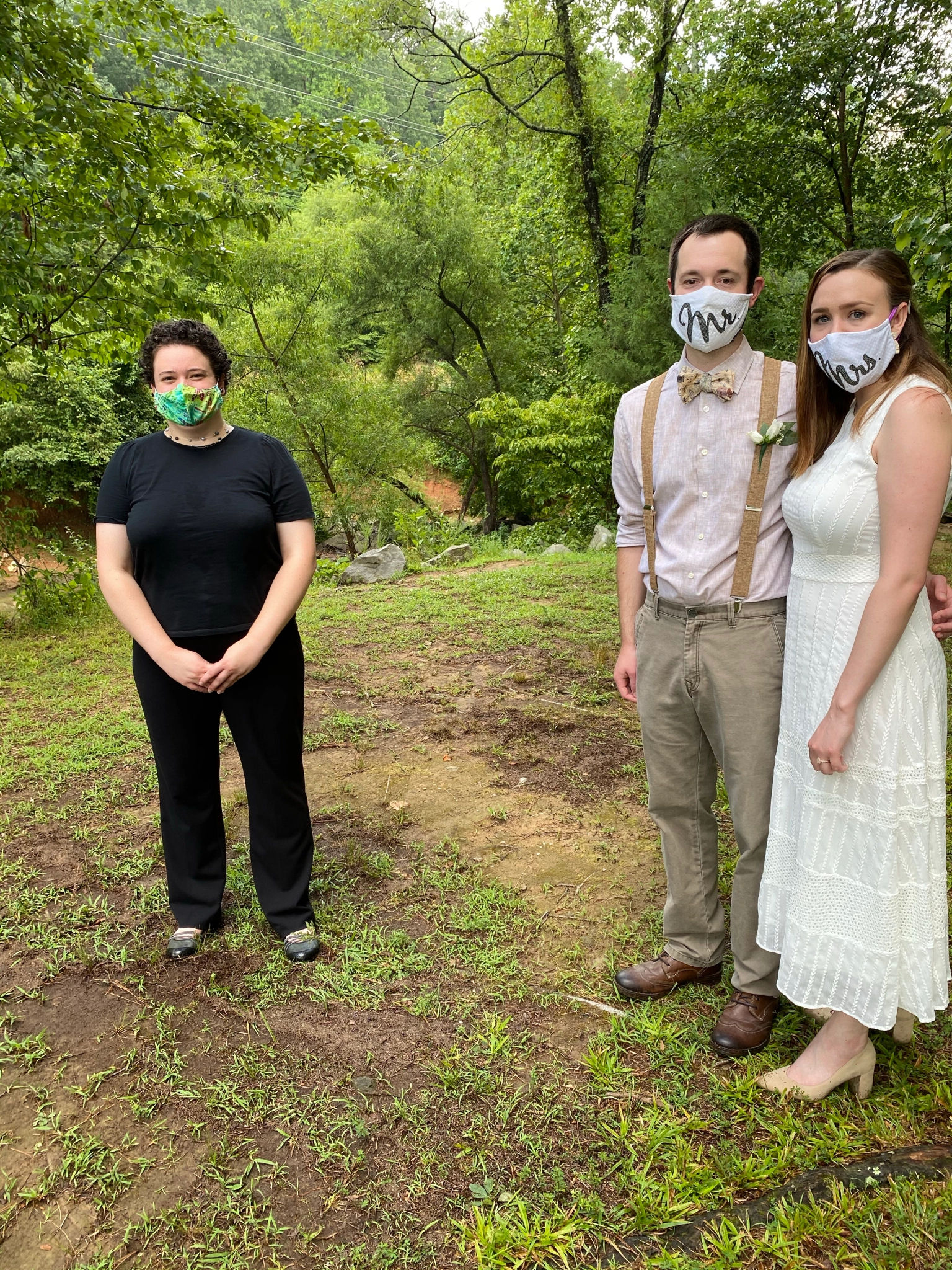 Carly, Drew, and Kayla standing in Umstead Park, greenery in the background, they’re all wearing masks, but smiling with their eyes