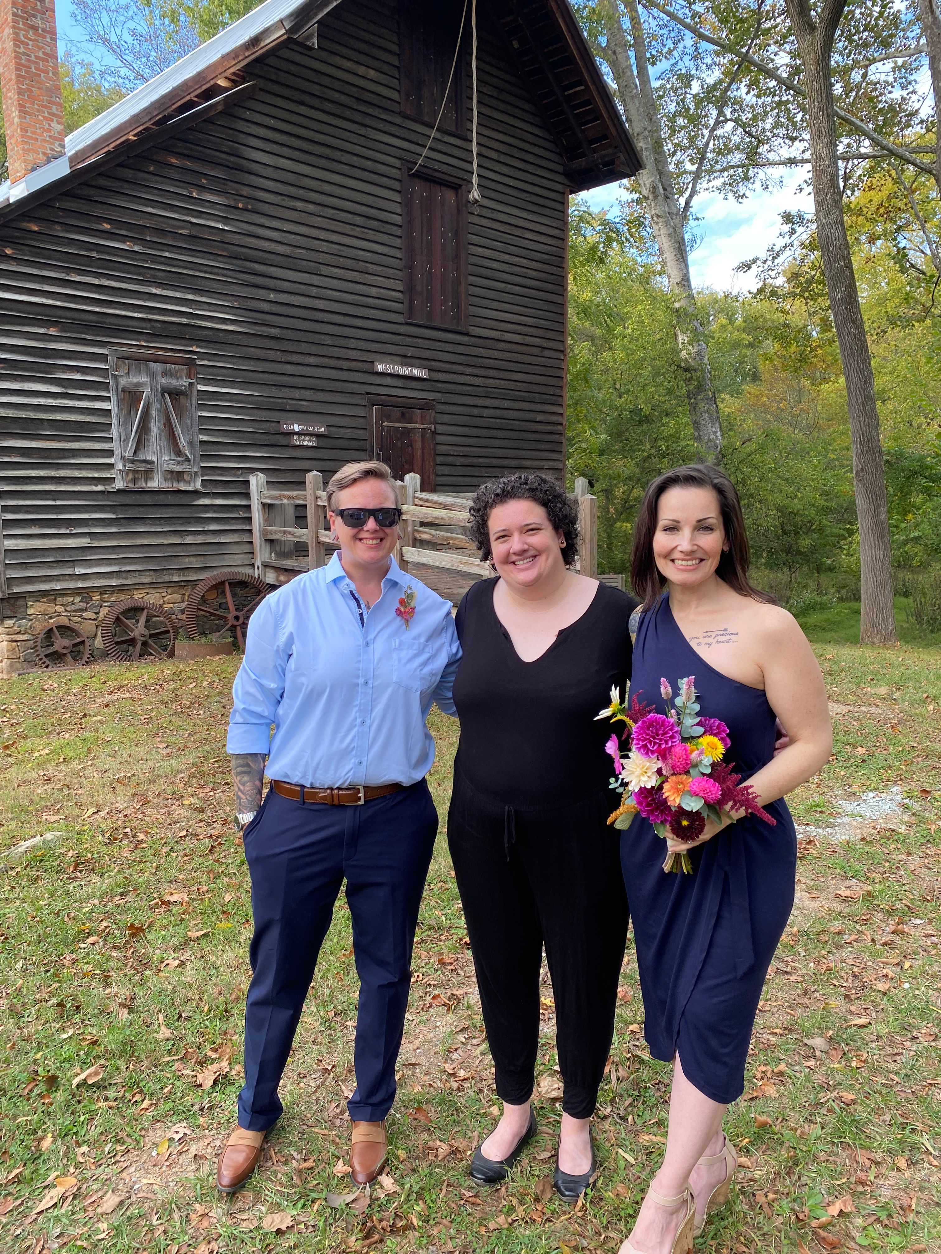 Ashley, Carly, and Amanda stand smiling with the old saw mill in the background 