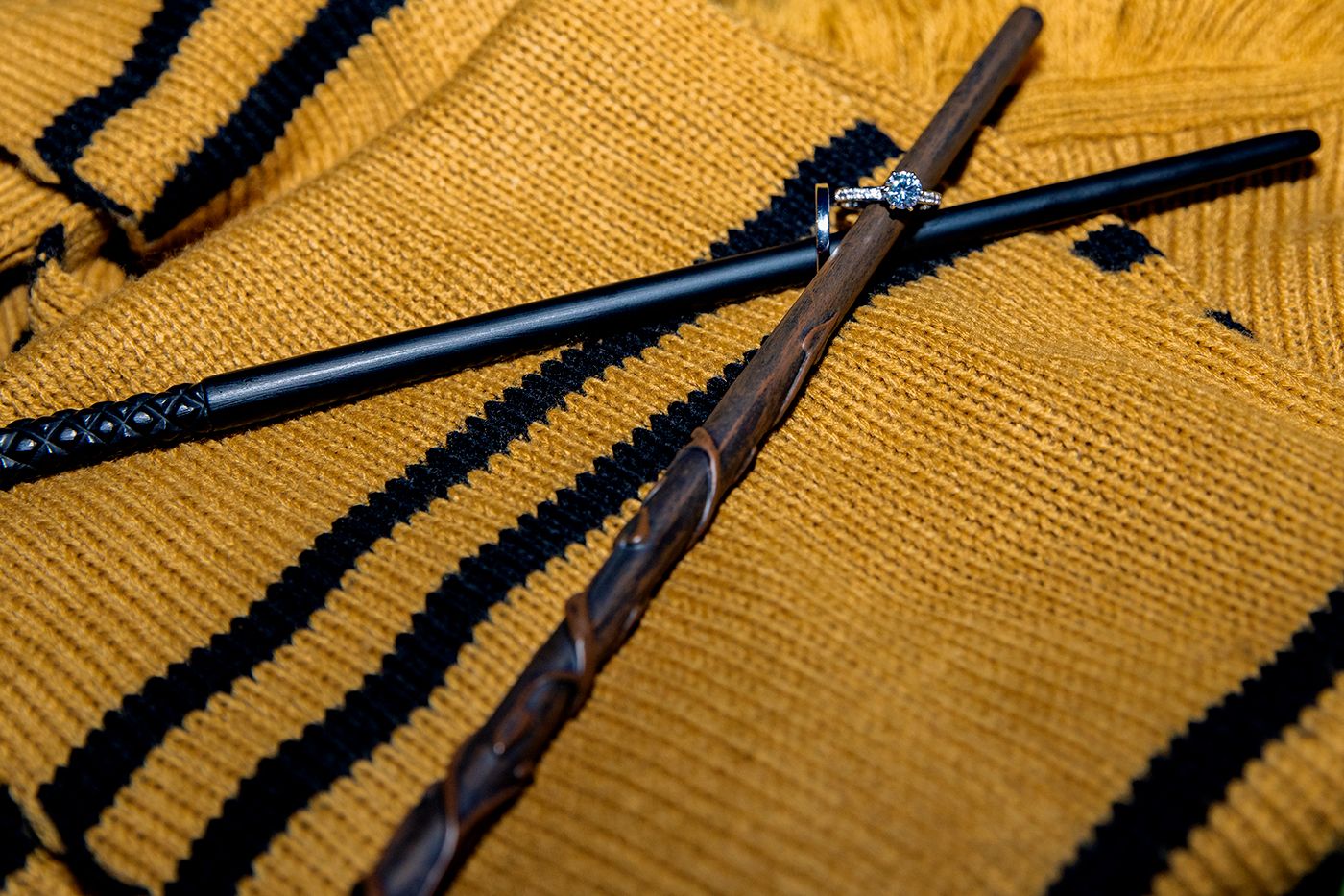 Two wands lay crossed on a Hufflepuff scarf with wedding rings around the tips of each.