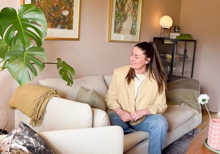 Helene sitter i sin beige sofa og forteller om boligkjøpsprosessen med Finit. 