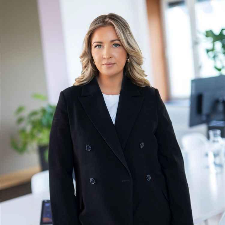 Portrett av Trine, ikledd sort blazer i et kontormiljø. 
